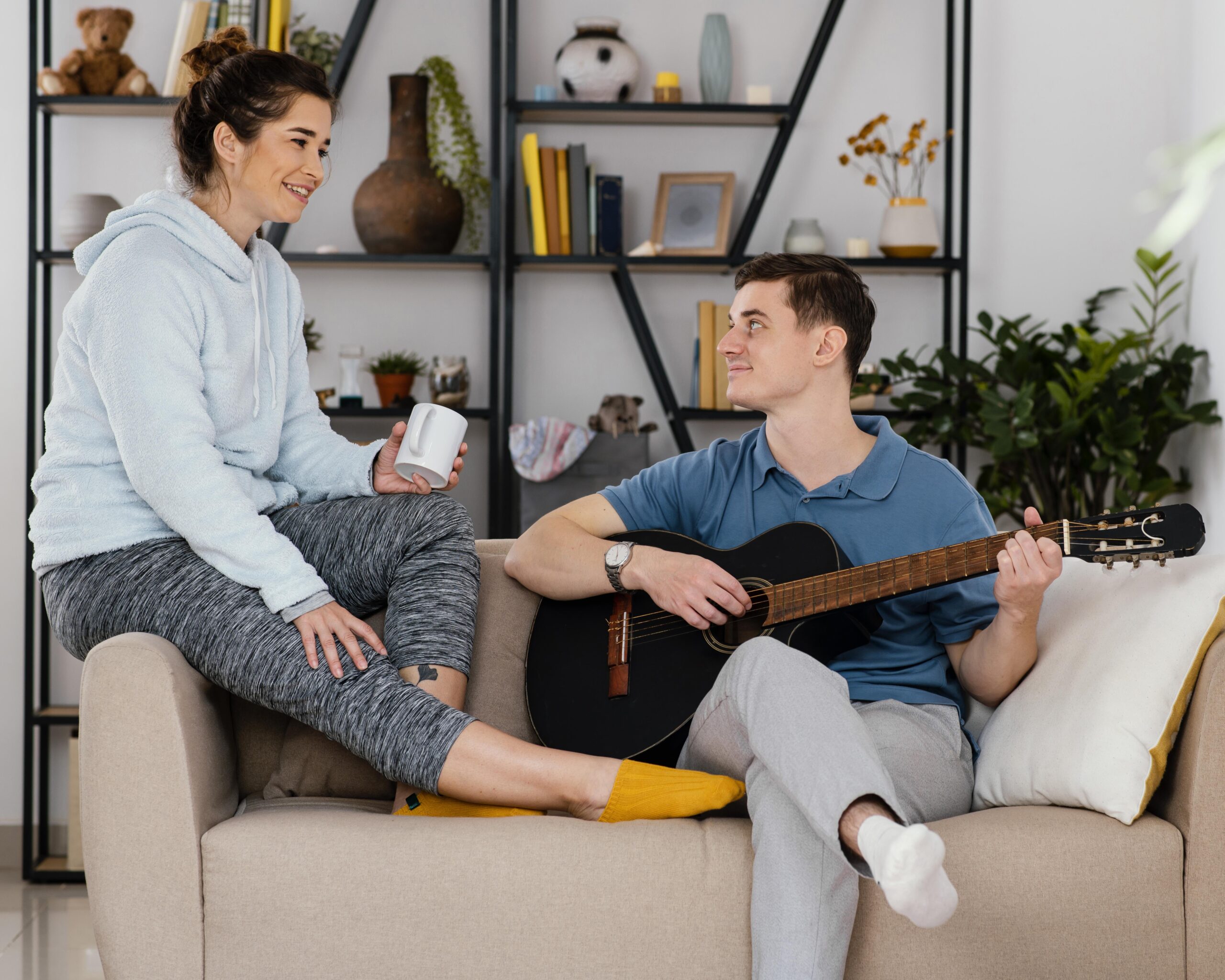 Two people talking on a sofa, one holding a guitar